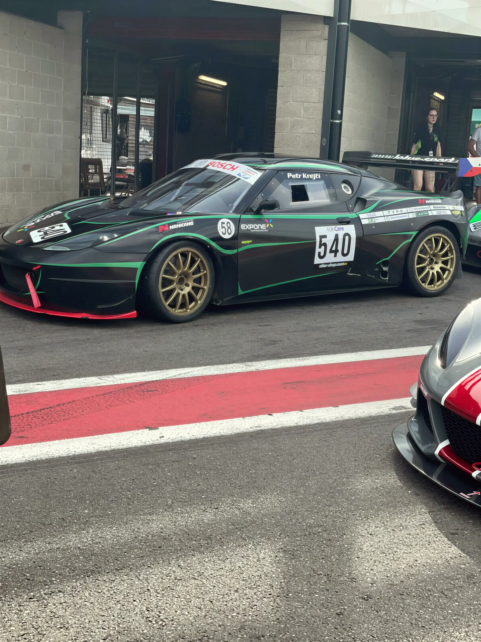 Evora 540 černo-zelená v pit lane, mokro, Spa-Francorchamps