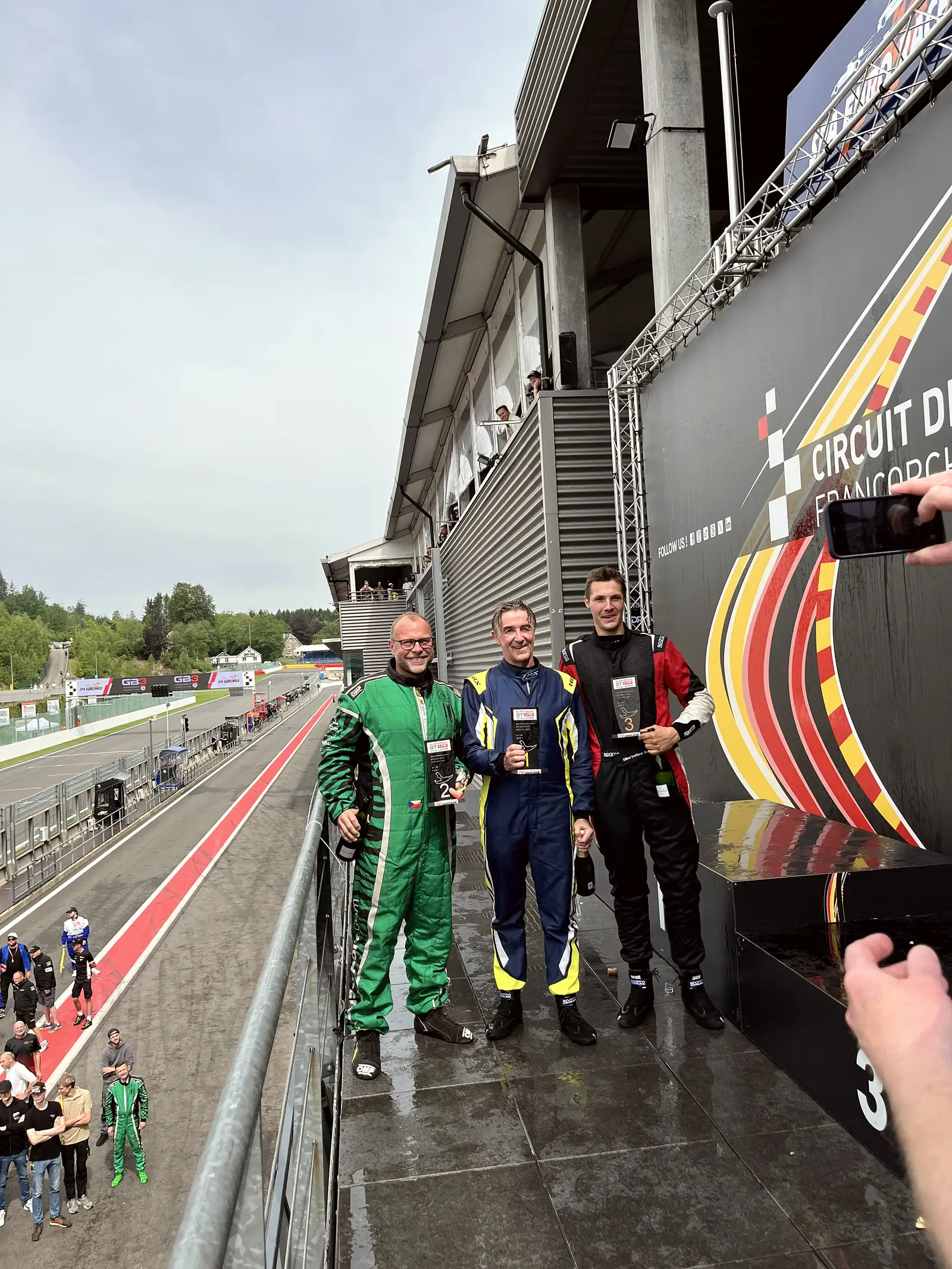 Stupně vítězů 2. místo, dva jezdci v kombinézách, cedule Circuit de Spa, Spa-Francorchamps